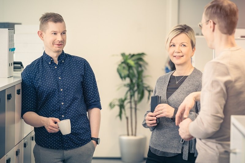 Kaksi miestä ja nainen seisovat rennosti ja juttelevat toimistohuoneessa.